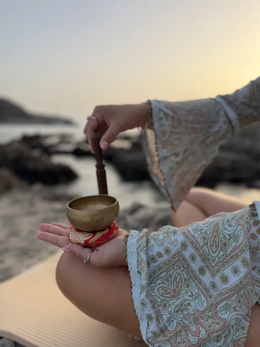 Hand mit Klöppel über einer Klangschale am Meer